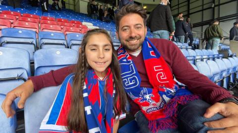 Young football fan Sophia sits with Newsround presenter Ricky in the stands
