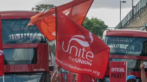A Unite the Union flag waves outside at a picket line near some buses