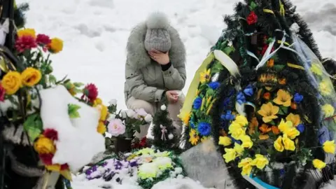 A woman reacts as she sits in front of a grave at a local cemetery, decorated with flowers to pay tribute to the victims of the Russian attack on Ukraine, on the day marking the fourth anniversary of the full-scale Russian invasion, in Chernihiv