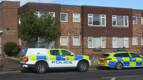 Two police vehicles are parked outside a two-storey residential building