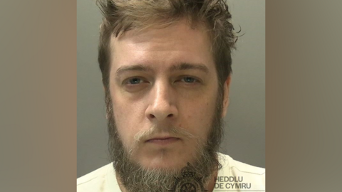 A custody image of a man with a beard and a whispy moustache 