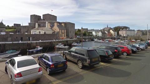 Castletown Harbour, with Castle Rushen in the background and a row of cars cars in the foreground.