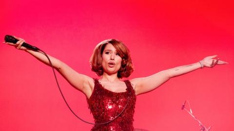 Singer Raye with her arms outstretched on stage