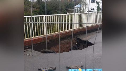 A hole in a bridge carriageway captured through a metal fence