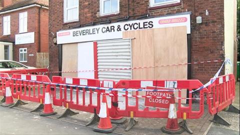 A police cordon around the front of the bike shop which has all its smashed windows and doors covered by wood panels