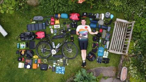 Simon Watts laying down in a garden surrounded by various items laid out next to his bike.