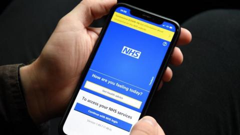 Person holding phone with NHS app displayed - largely blue screen with the NHS logo on it