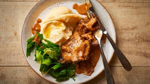 Slow cooked beef cheeks with creamy mash and greens on a white plate