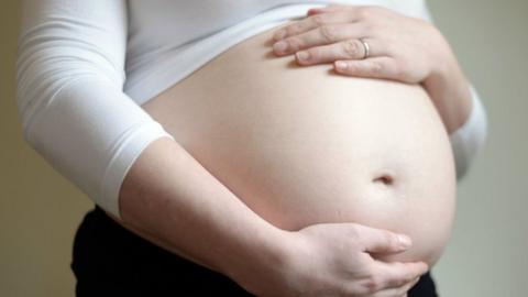 File photo of a woman wearing a white shirt holding a pregnant stomach.