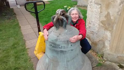 Tudor-era tenor bell outside the church and being hugged by a woman, Landbeach