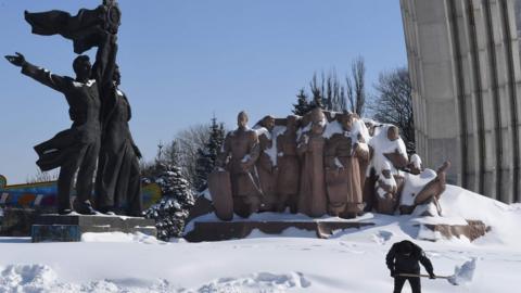 A communal worker cleans a road from a snow in front of Soviet era monument Ukraine and Russia union in Ukrainian capital of Kiev after heavy night snowfall on March 2, 2018