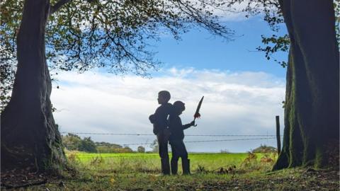 Two children standing back to back between trees on Staple Hill in Somerset