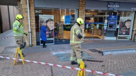 smashed glass on floor outside bank with fire crew around