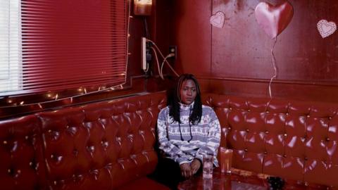 Kym sits in the corner of a nightclub with red walls and sofas