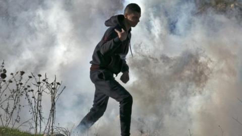 A Palestinian protestor runs for cover from tear gas fired by Israeli security forces during clashes in the West Bank