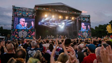 People cheering in front of a stage where Suggs is performing