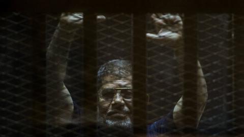 Ousted Egyptian president Mohamed Morsi gestures from the defendants cage as he attends his trial at the police academy on the outskirts of the capital Cairo