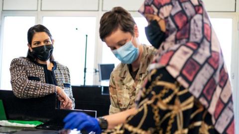 Priti Patel watches an Afghan refugee give her fingerprints during processing at Heathrow