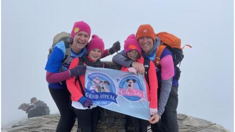 Kara pictured with her mum Sarah, sister Isobel and Dad Stephen at the summit of Snowdon. They are holding a grand appeal flag.