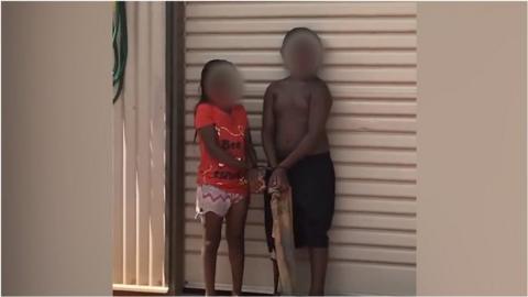 Two children stand in front of a garage door