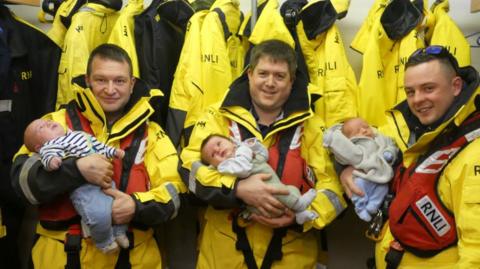 Three RNLI volunteers holding their newborn babies