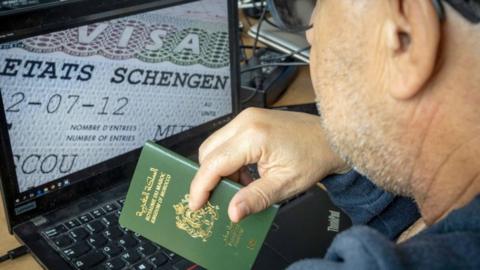 Man holding passport with photo of visa on laptop