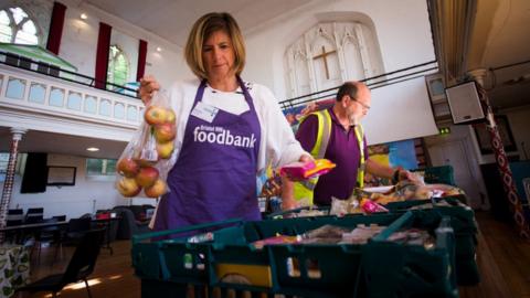 A woman wearing a purple apron working at a Foodbank