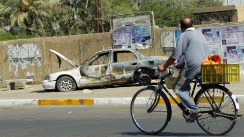 An Iraqi man rides a bicycle passing by a remains of a car burnt during a deadly incident involving Blackwater guards in Baghdad in September 2007