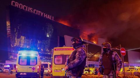 Law enforcement officers stand guard near the burning Crocus City Hall concert venue following a shooting incident, outside Moscow, Russia, March 22, 2024