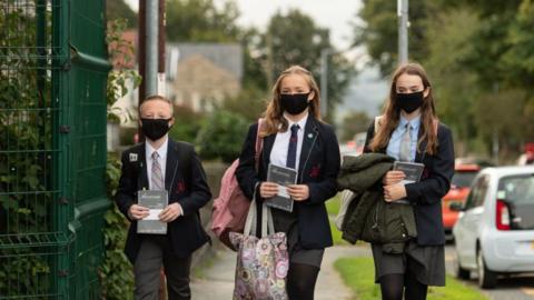 Children wearing face coverings enter a school