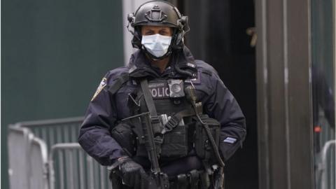 An armed officer in New York City stands guard outside Trump Tower wearing a face mask