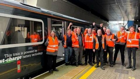 Great Western Railway employees in orange hi-vis jackets standing next to a battery-powered train