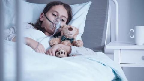 child in hospital bed cuddling a teddy bear