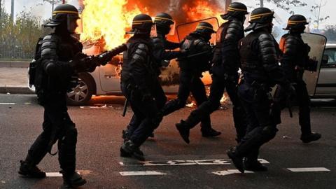 French riot police walk past a burning vehicle during yellow vests protests