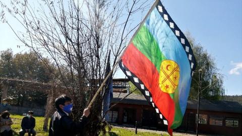 A Mapuche indigenous person holds up a Mapuche flag