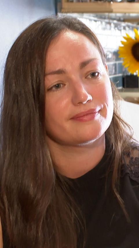 Close up of Cat, Linda and Razzell's daughter. She is wearing a black top and is sat near a kitchen