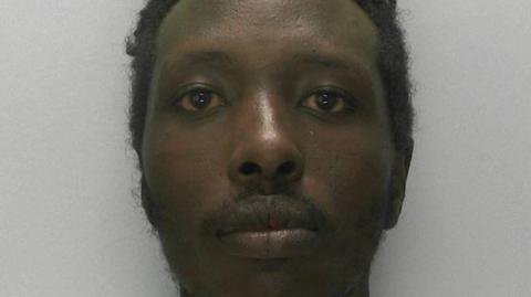 A bearded man looking at the camera in a police mugshot