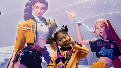 A girl in a KPop Demon Hunters costume standing in front of a still from the film