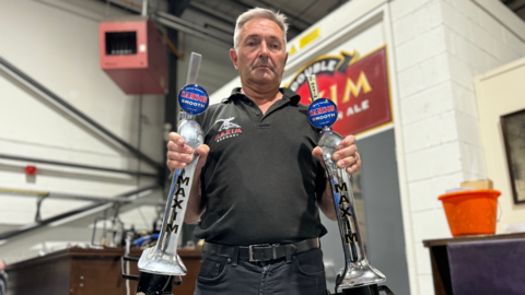 A man stands holding two beer pumps removed from a bar