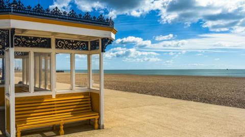 Covered seating area on a prom next to a beach with mainly blue skies above 