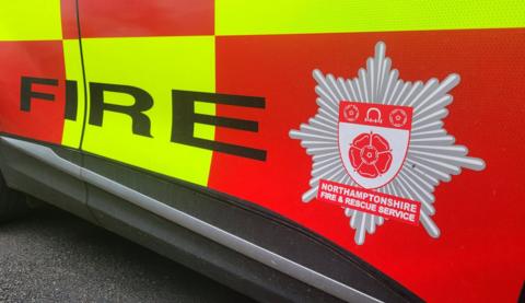 The side of a fire vehicle, with a county's fire sign on it. There are blocks of red and yellow on the vehicle.