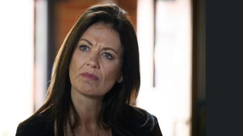 Monica Harding, a middle aged woman with long brown hair, concentrates on something in the middle distance.