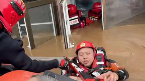 A man, wearing a red life jacket, is rescued from a Beijing nursing home inundated with chest-high flood water.