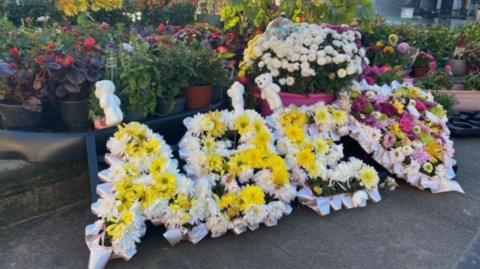 Floral tributes include the letters A, B and E, and a floral heart, along with teddies.