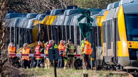 Two trains collided against each other as emergency services stand outside the crash.