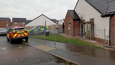 A fire care and police car sit outside a red brick and white house where scorch marks can be seen