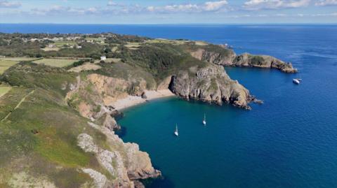 A picture taken from above, looking down on the island of Sark. There are a number of boats around the island, with sand beaches.