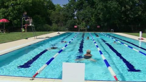 People swimming in lanes at Abbey Meadows outdoor pool, whilst a lifeguard looks on