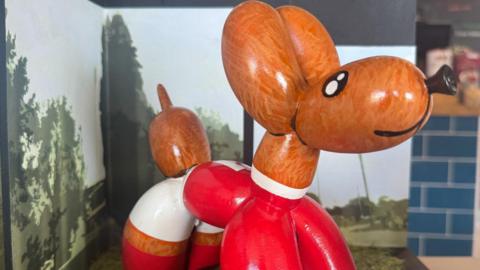 A mini balloon dog sculpture painted wearing a red football kit