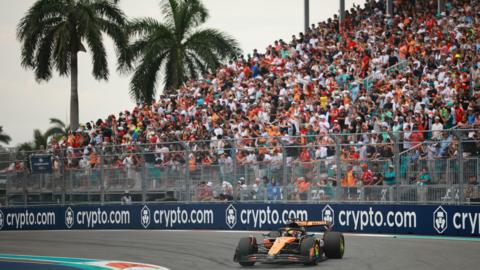 McLaren's Oscar Piastri turns into a right-hand corner during the 2025 Miami Grand Prix. A packed grandstand and two palm trees are in the background